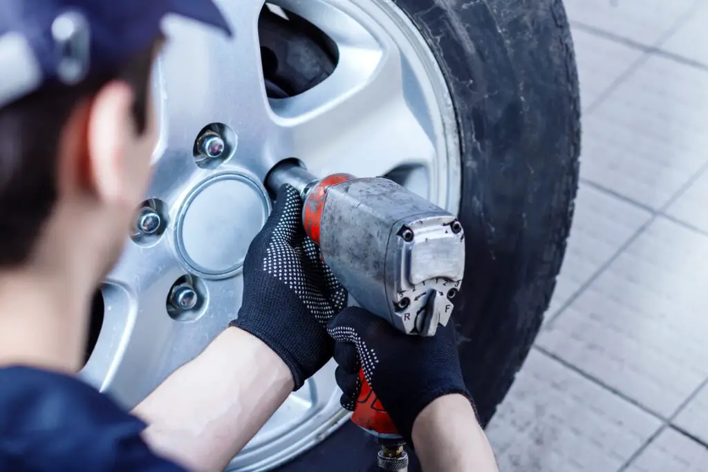 A mechanic using a power tool to change a car tire in an auto repair shop.